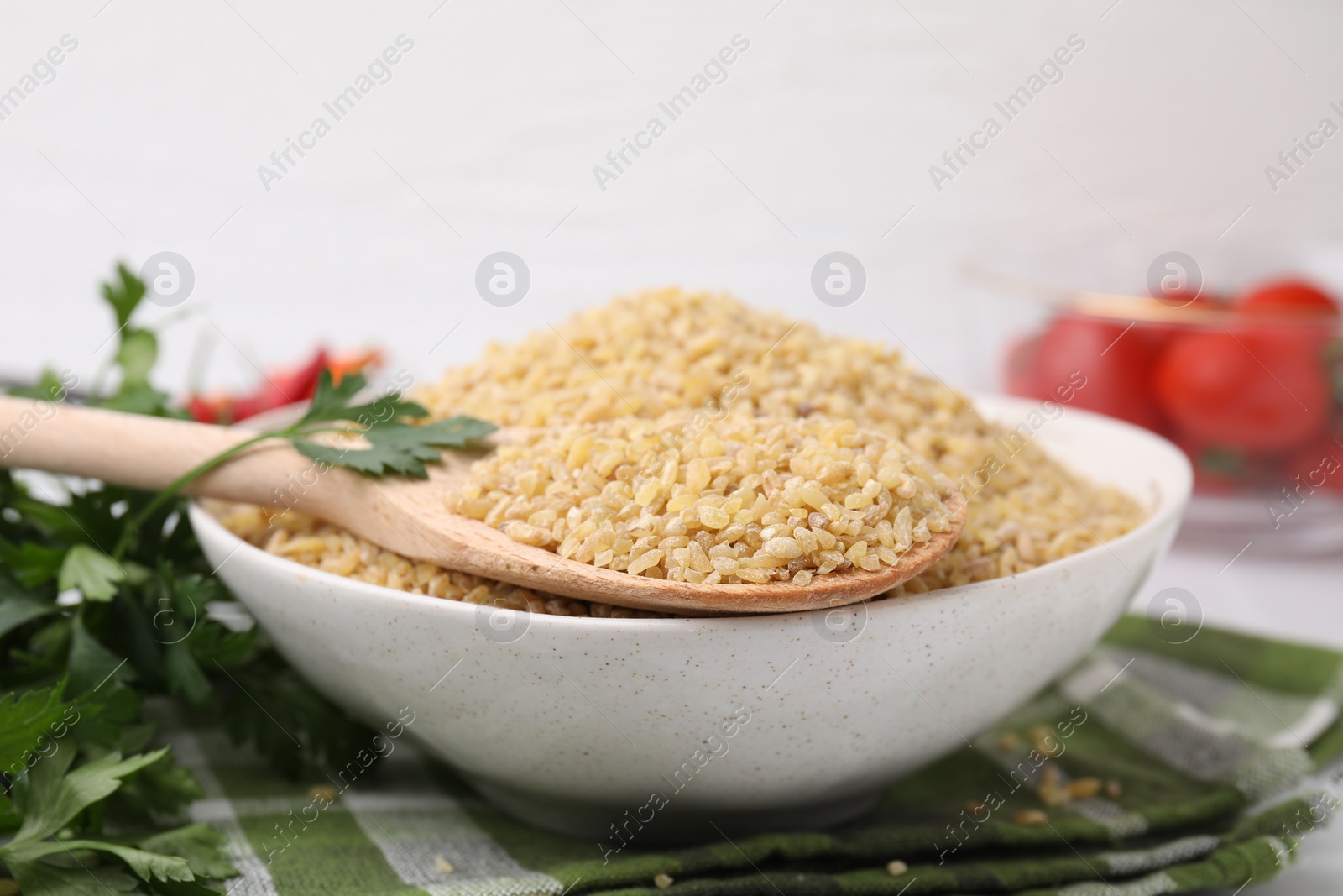 Photo of Bowl and spoon with raw bulgur on table, closeup