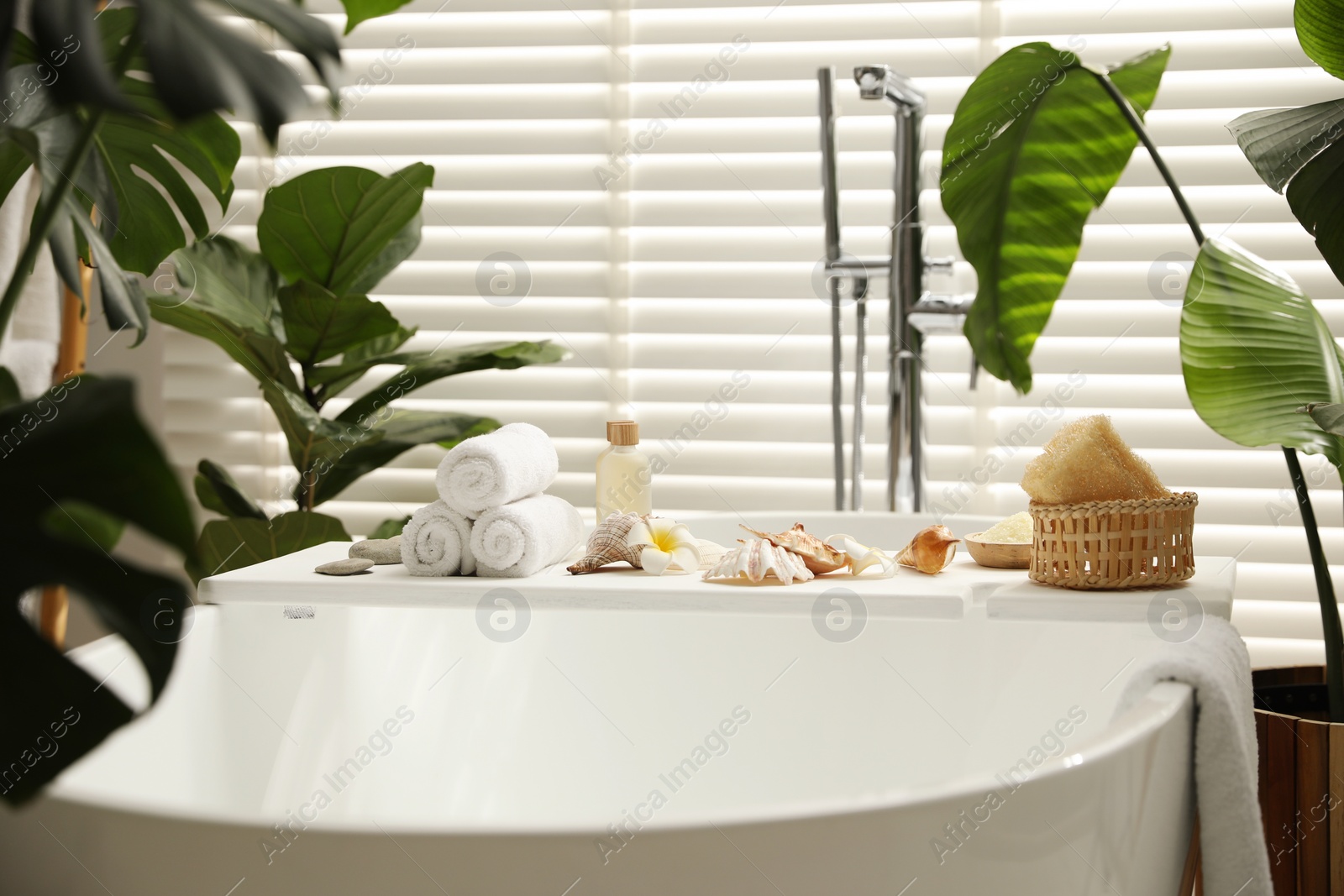 Photo of Bath tray with spa products, towels and shells on tub in bathroom