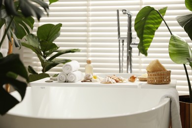 Bath tray with spa products, towels and shells on tub in bathroom