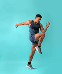 Photo of Athletic young man running on turquoise background, side view