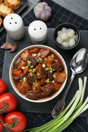 Photo of Delicious beef stew with carrots, green onions and ingredients on grey table, flat lay