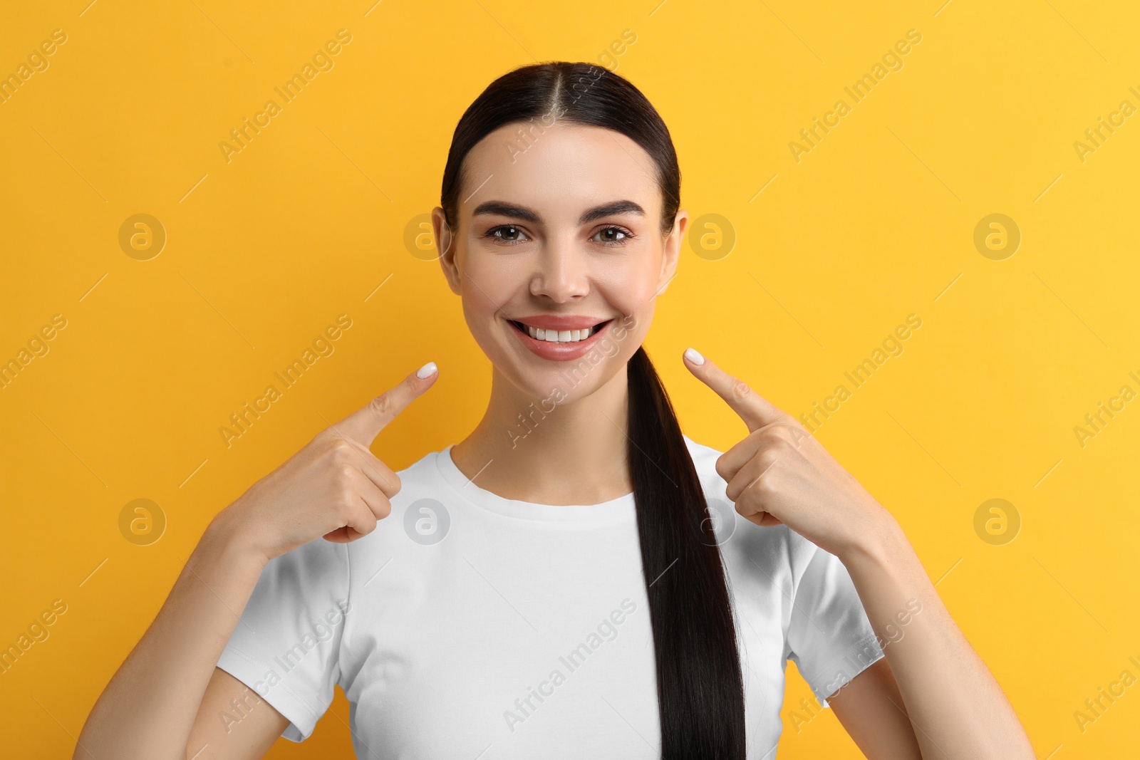 Photo of Beautiful woman showing her clean teeth and smiling on yellow background