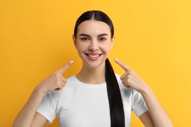Beautiful woman showing her clean teeth and smiling on yellow background