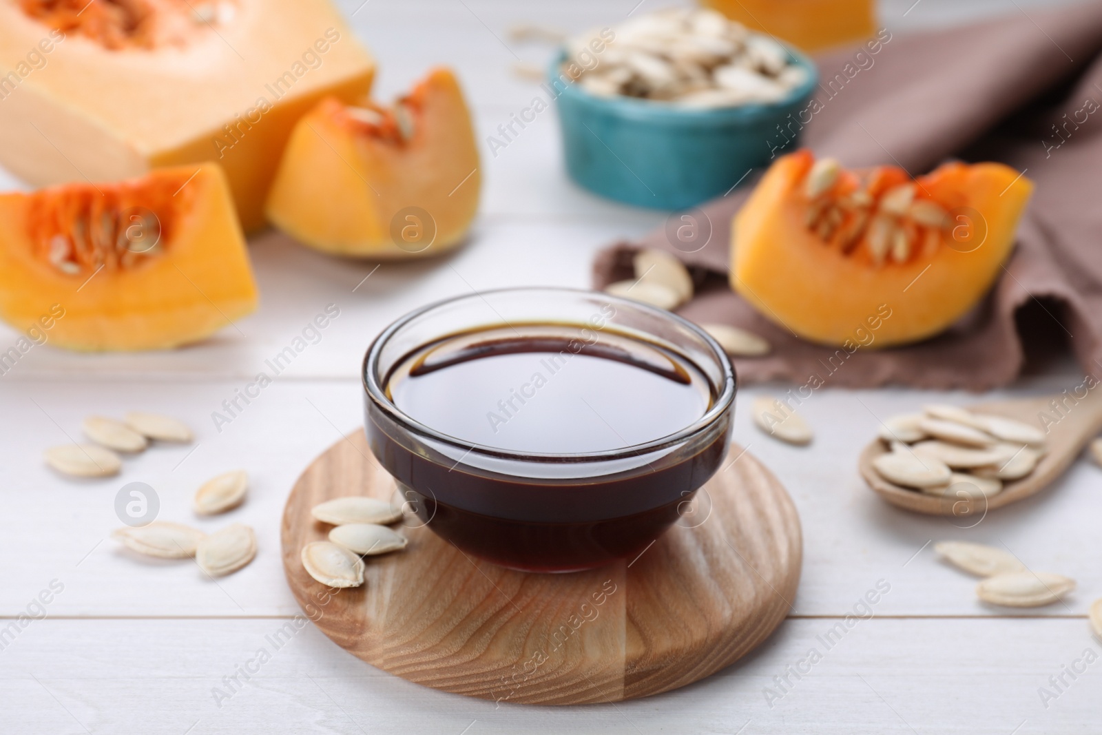 Photo of Glass bowl of fresh pumpkin seed oil on white wooden table