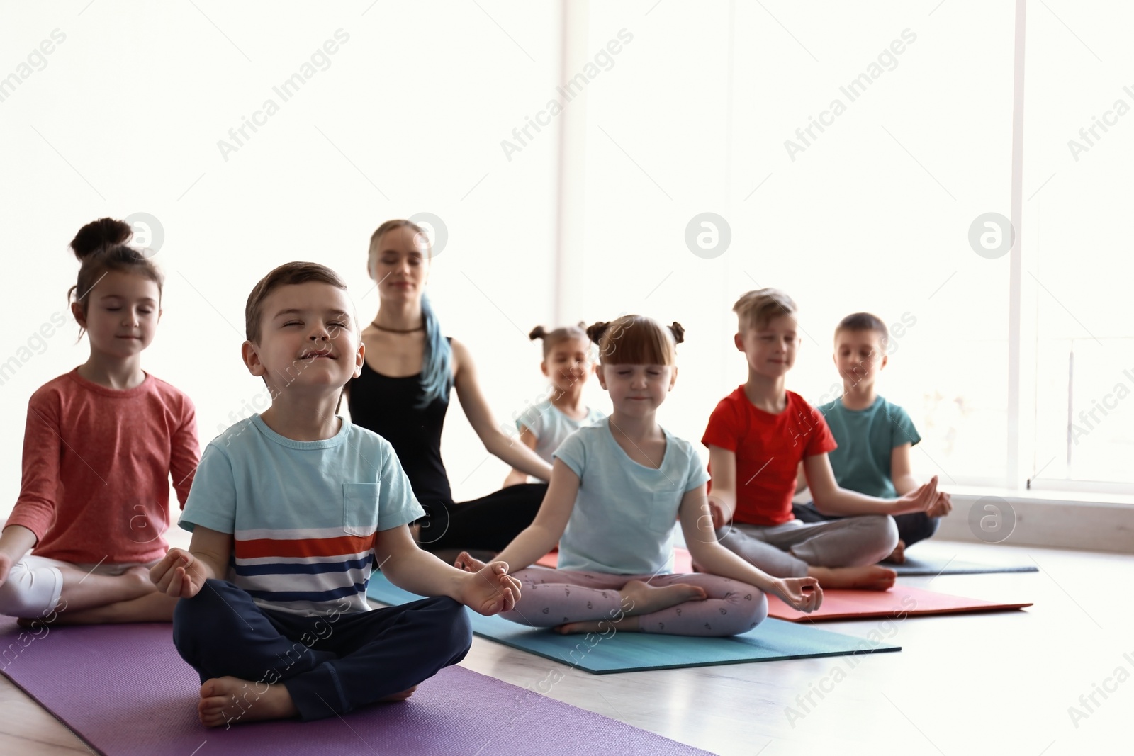 Photo of Little children and their teacher practicing yoga in gym