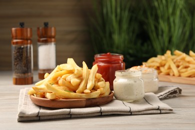 Delicious french fries served with sauces on light wooden table, closeup