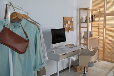 Photo of Stylish room interior with comfortable workplace and rack of clothes