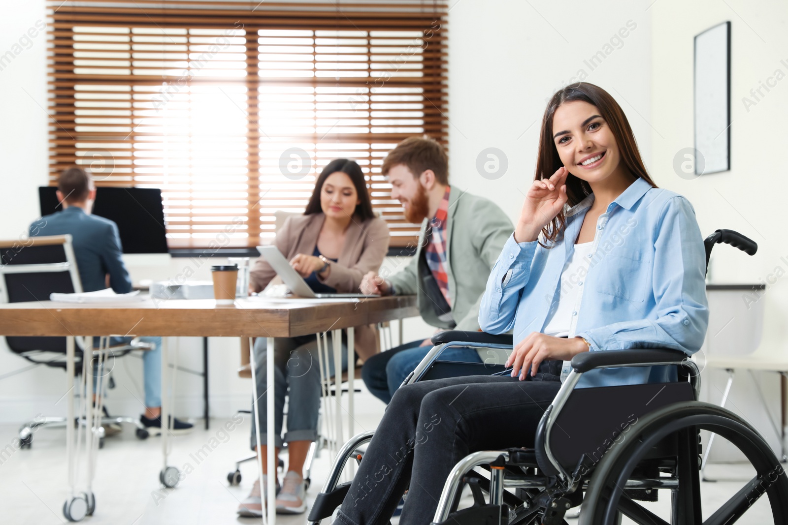 Photo of Young woman in wheelchair with colleagues at office