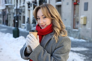Portrait of charming woman with paper cup of coffee on city street in winter