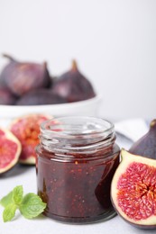 Glass jar of tasty sweet fig jam and fruits on light table