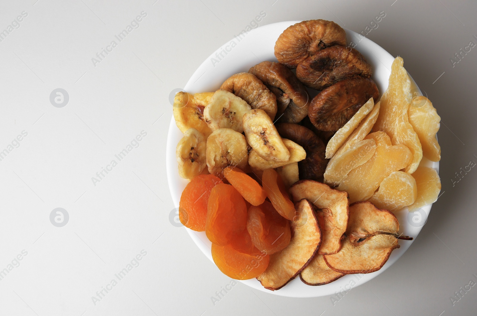 Photo of Bowl of different dried fruits on white background, top view. Space for text