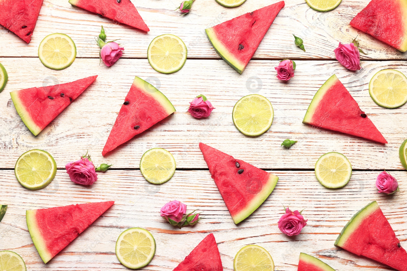 Photo of Tasty sliced watermelon, roses and limes on white wooden table, flat lay