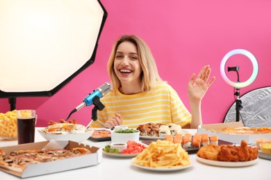 Photo of Food blogger recording eating show near microphone at table against pink background. Mukbang vlog