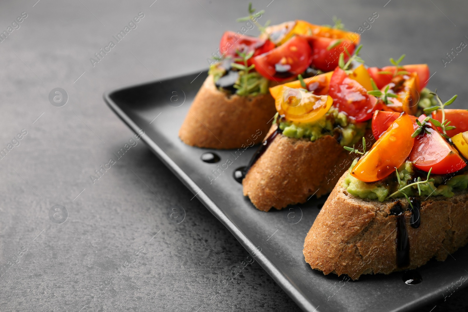 Photo of Delicious bruschettas with avocado, tomatoes and balsamic vinegar on gray table, closeup. Space for text