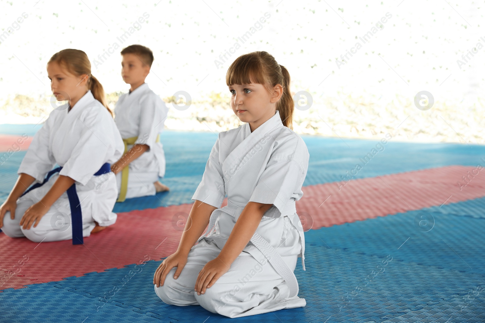 Photo of Children in kimono sitting on tatami outdoors. Karate practice
