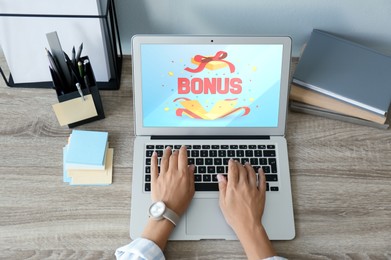 Image of Bonus gaining. Woman using laptop at wooden table, above view. Illustration of open gift box, word and confetti on device screen