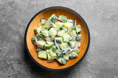 Photo of Wooden dish with fresh creamy cucumber salad on table, top view