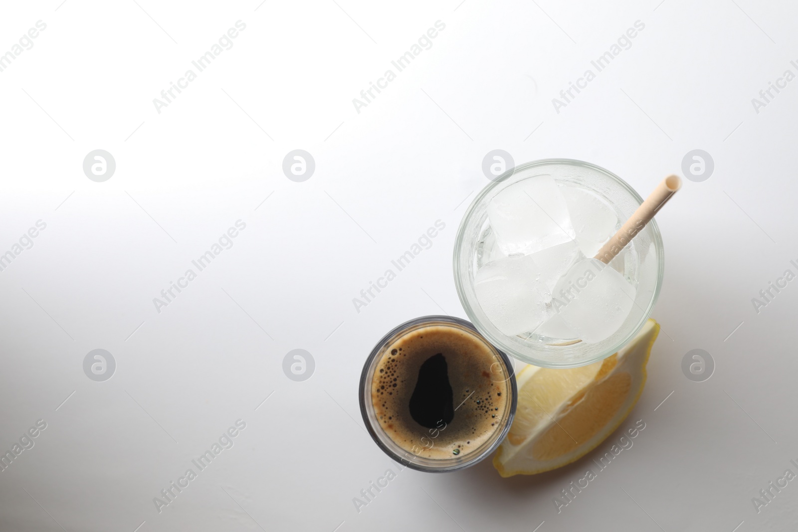 Photo of Coffee and ice cubes in different glasses, cut lemon on white background, top view