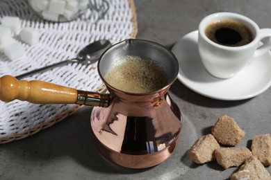 Turkish coffee. Cezve and cup with hot aromatic coffee and sugar on grey table