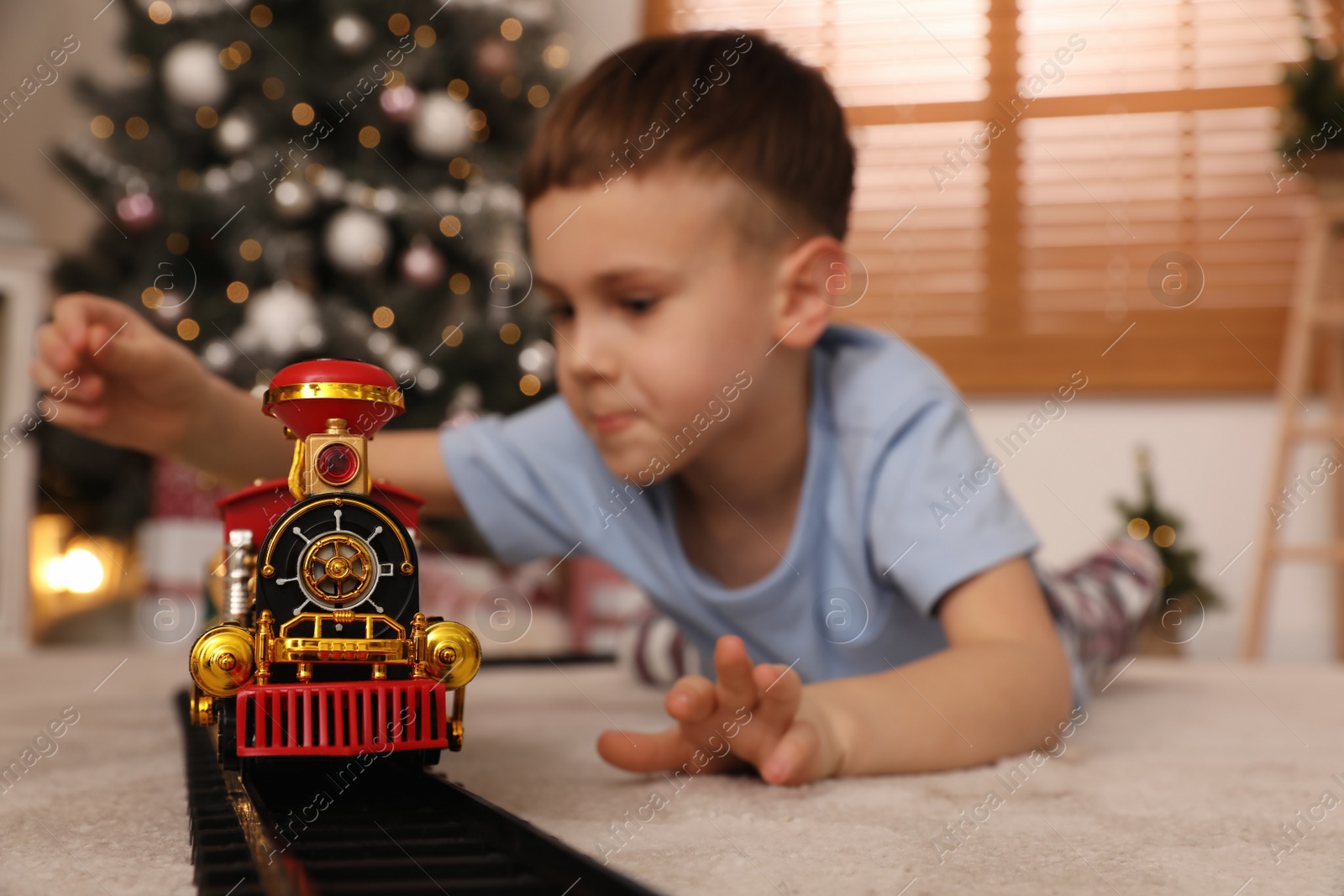 Photo of Little boy playing with colorful toy in room decorated for Christmas, focus on train