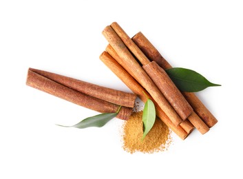 Photo of Dry aromatic cinnamon sticks, powder and green leaves isolated on white, top view