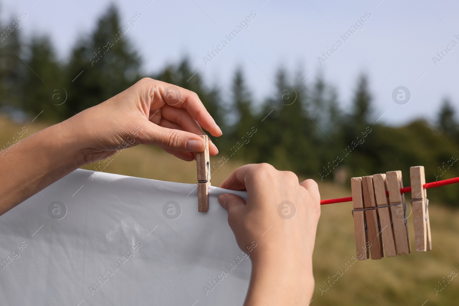 Photo of Woman hanging clean laundry with clothespins on washing line outdoors, closeup