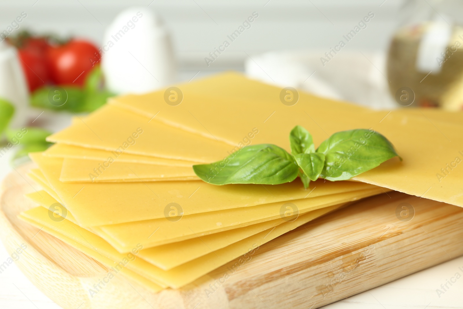 Photo of Uncooked lasagna sheets and basil on white wooden table, closeup