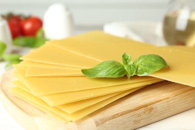 Photo of Uncooked lasagna sheets and basil on white wooden table, closeup