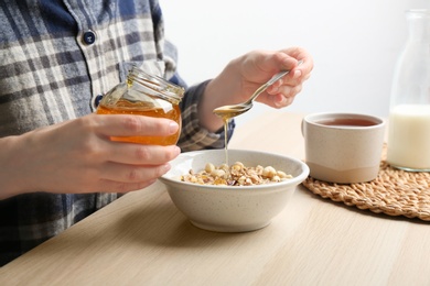 Photo of Woman putting honey into bowl with muesli at wooden table, closeup