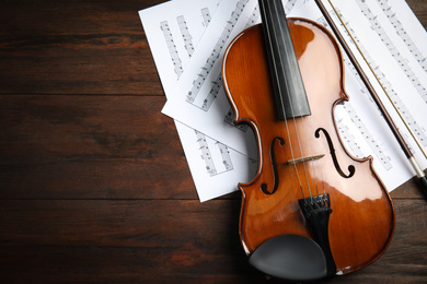 Photo of Beautiful violin, bow and note sheets on wooden table, flat lay. Space for text