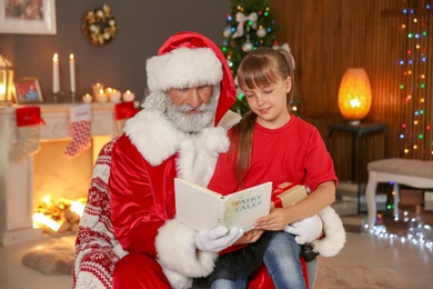 Photo of Little child with Santa Claus reading Christmas story at home