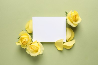 Beautiful yellow roses, petals and blank card on light olive background, flat lay. Space for text