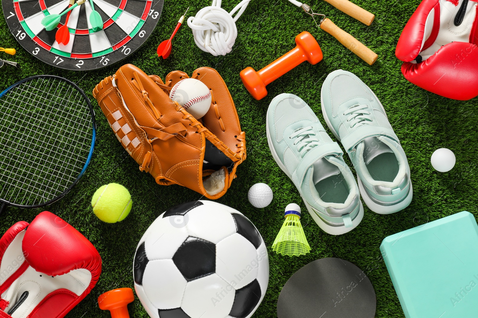 Photo of Different sport equipment and sneakers on green grass, flat lay