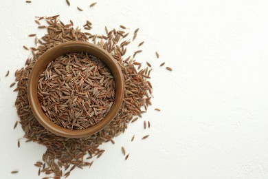 Photo of Caraway (Persian cumin) seeds and bowl on white table, top view. Space for text