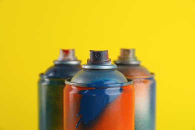 Photo of Used cans of spray paints on yellow background, closeup
