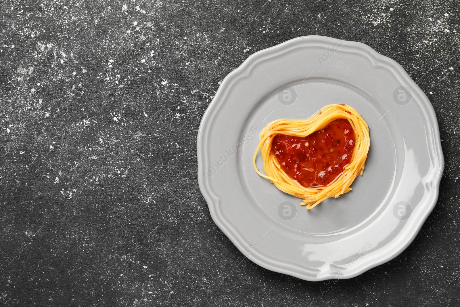 Photo of Heart made with spaghetti and sauce on black table, top view. Space for text