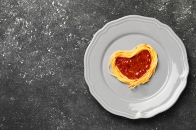 Heart made with spaghetti and sauce on black table, top view. Space for text