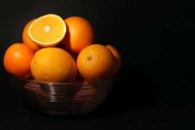 Bowl with ripe juicy oranges on black background. Space for text