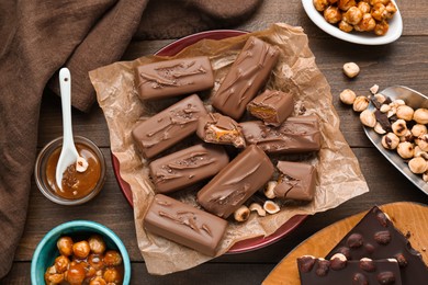 Photo of Delicious chocolate candy bars and nuts on wooden table, flat lay