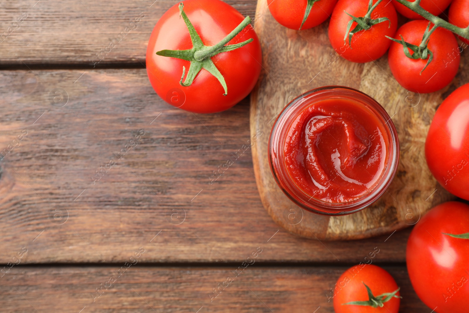 Photo of Jar of tasty ketchup and tomatoes on wooden table, flat lay. Space for text