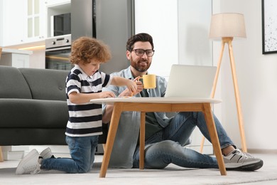 Photo of Man working remotely at home. Father using laptop while his son drawing at desk