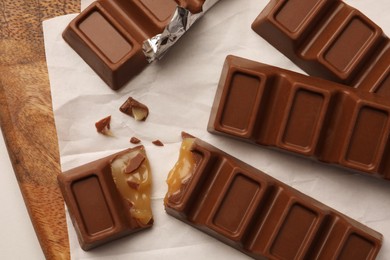 Tasty chocolate bars with wooden board on white table, top view