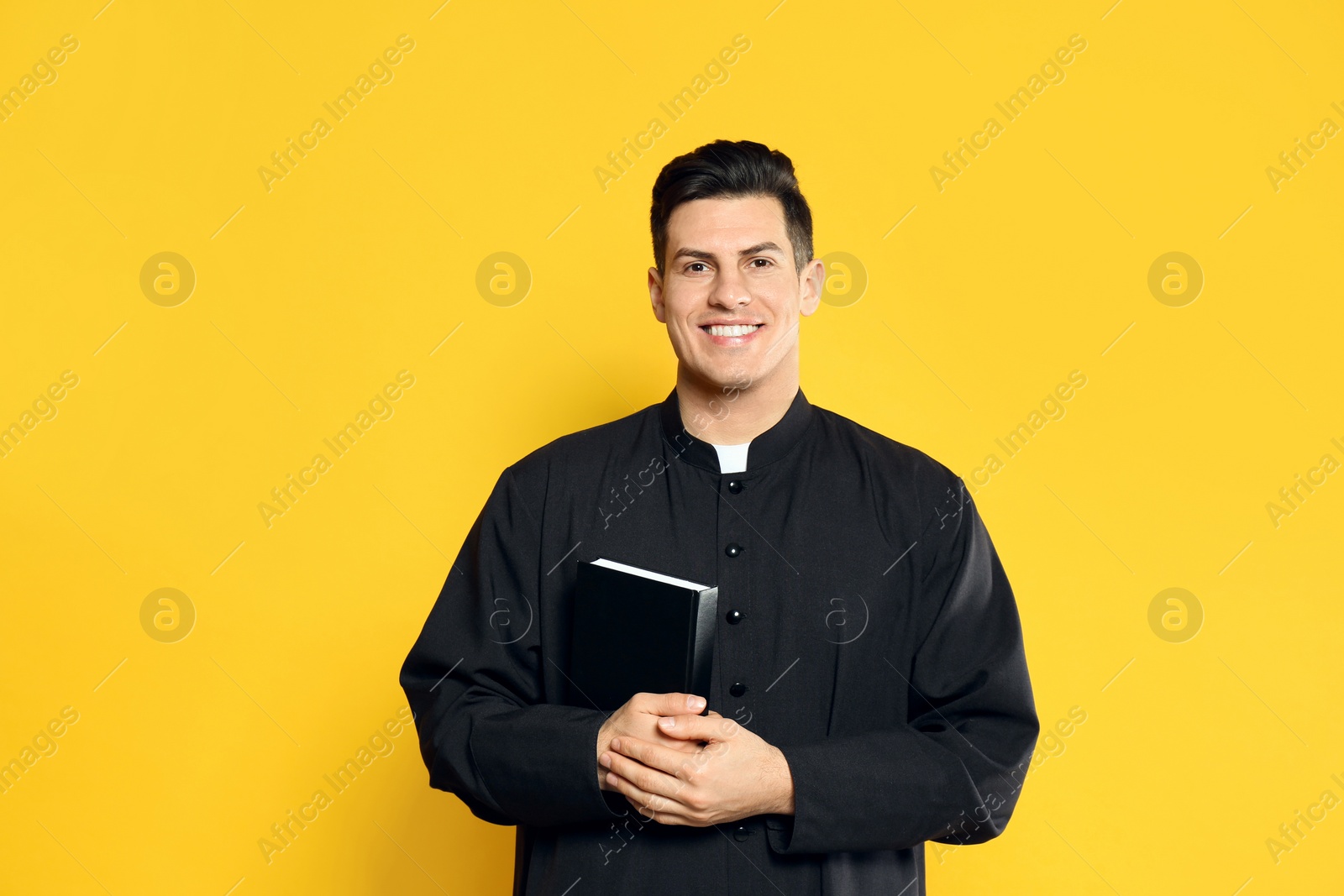 Photo of Priest in cassock with Bible on yellow background