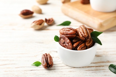 Tasty pecan nuts in dish on wooden table. Space for text