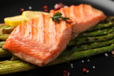 Tasty grilled salmon with asparagus and spices on plate, closeup