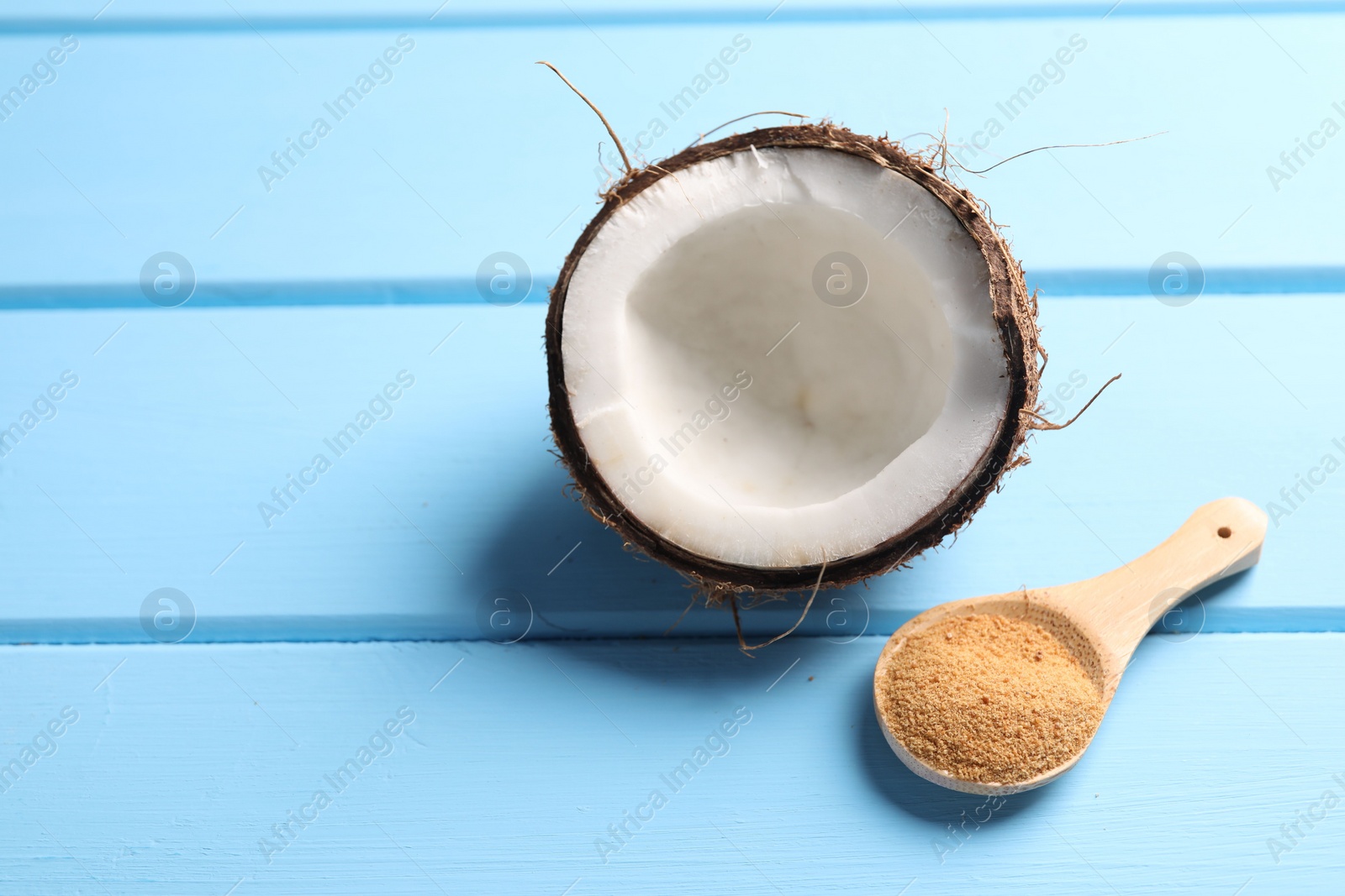 Photo of Spoon with coconut sugar and half of fruit on light blue wooden table, closeup. Space for text