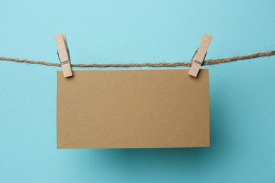 Photo of Wooden clothespins with blank notepaper on twine against light blue background. Space for text