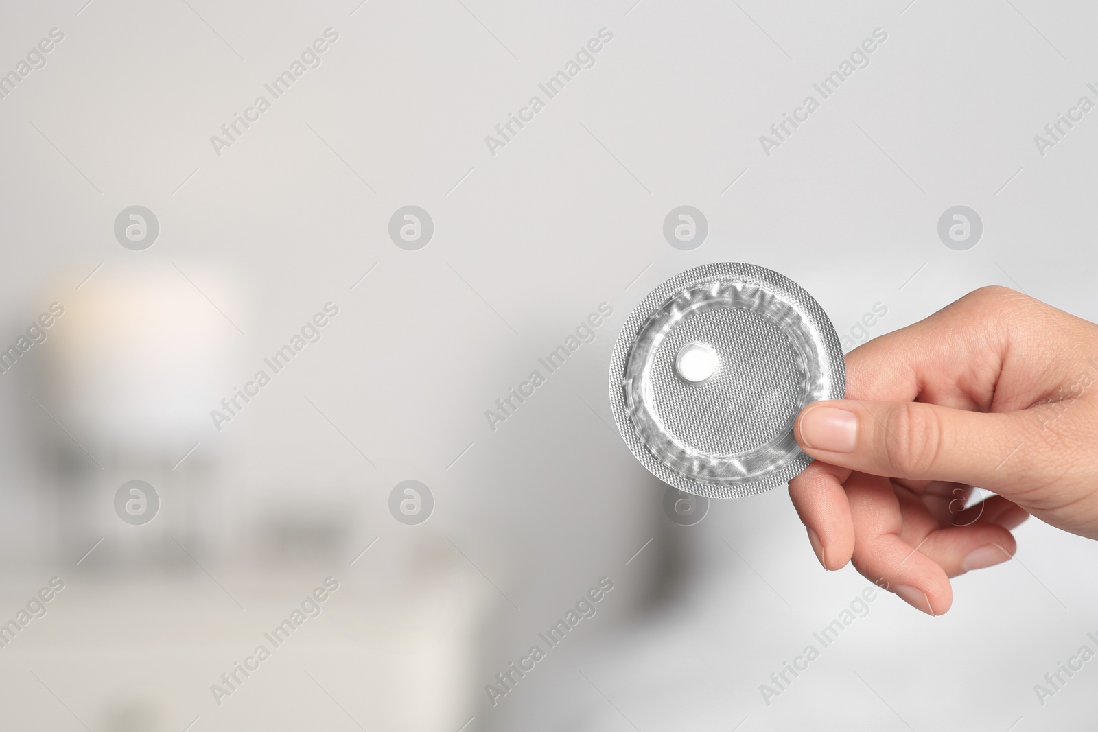 Photo of Woman holding blister of emergency contraception pill against blurred background, closeup. Space for text