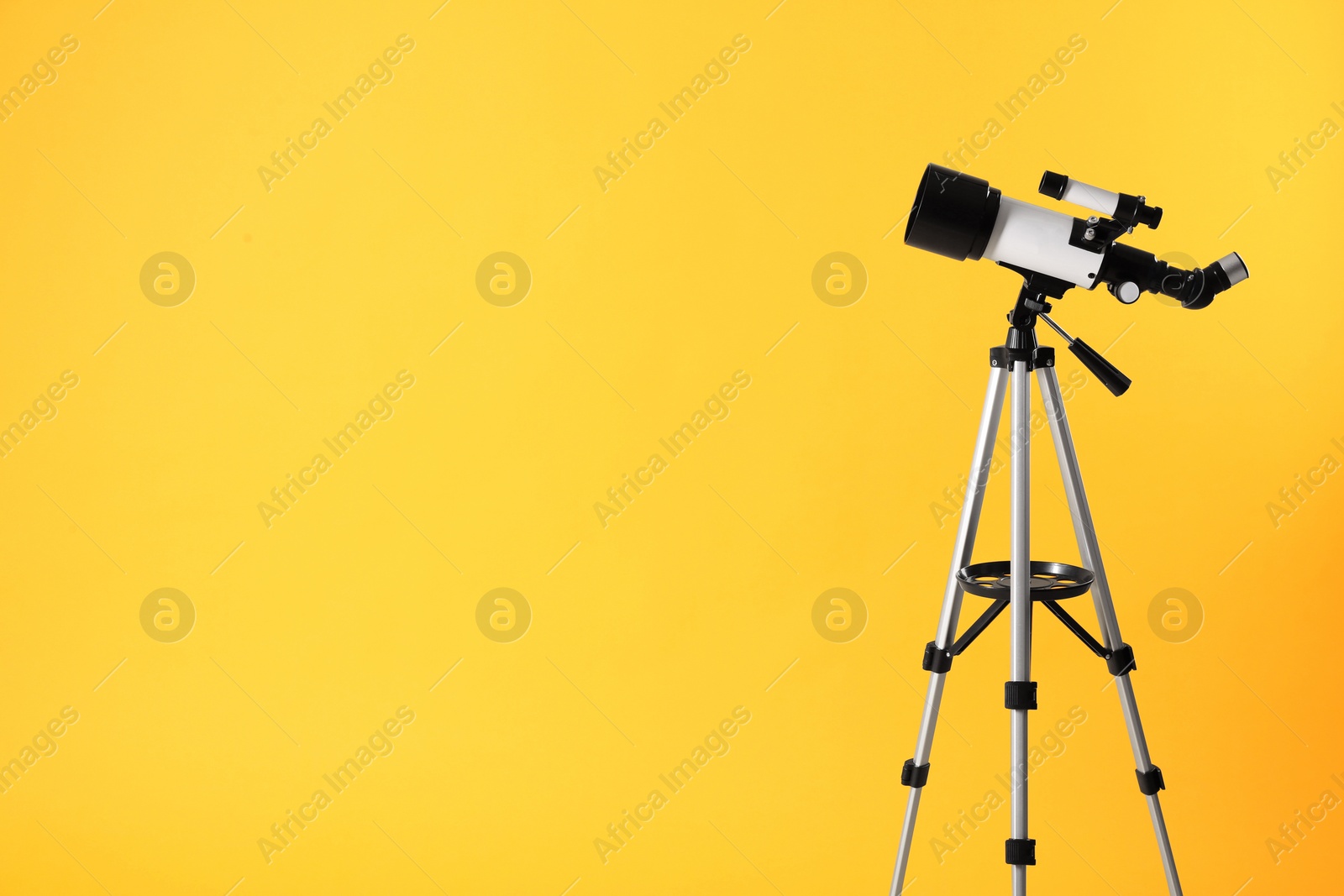 Photo of Tripod with modern telescope on yellow background. Space for text