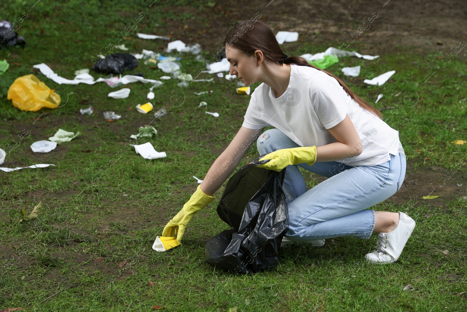 Photo of Young woman with plastic bag collecting garbage on green grass outdoors